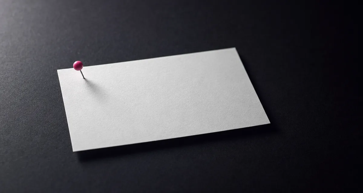 A blank off-white index card lying flat on a near-black surface, held down by a single magenta push-pin.